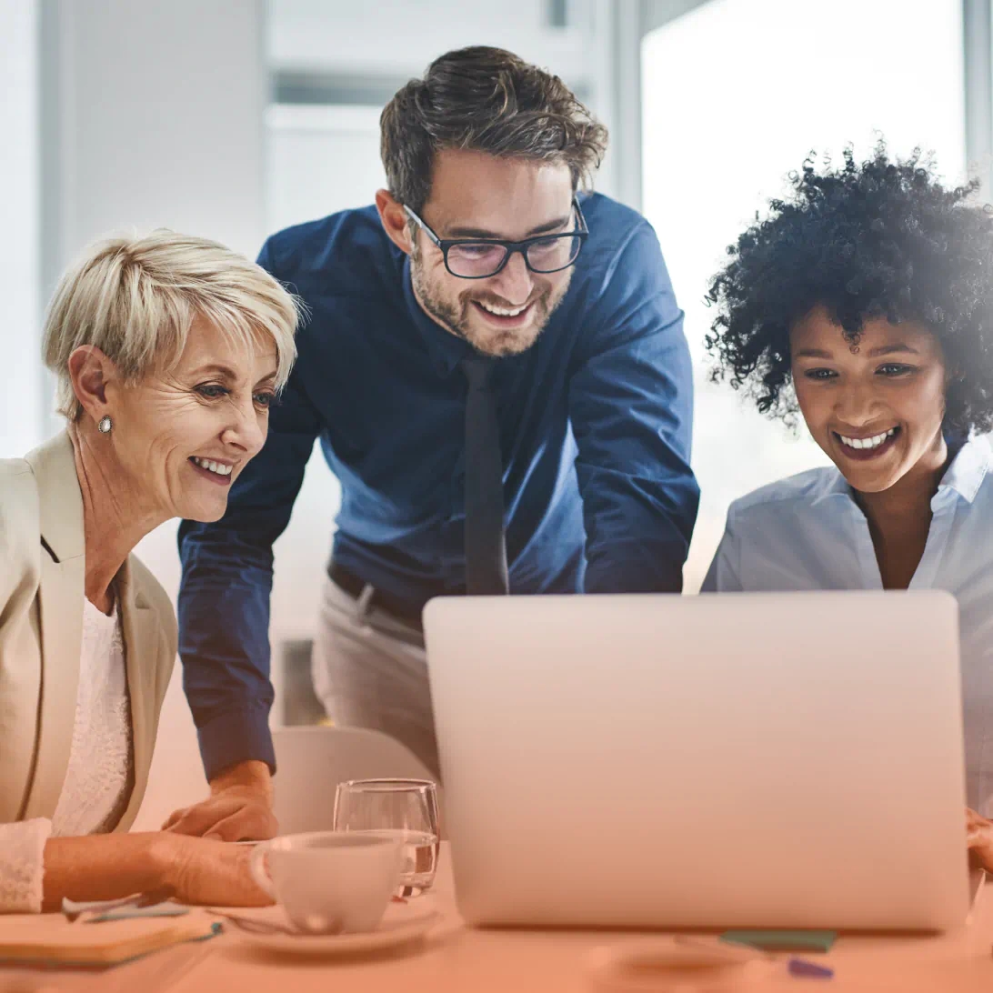 Three people smile while looking at a laptop