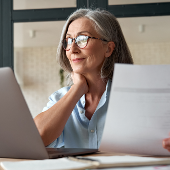 Woman holding paper and using laptop