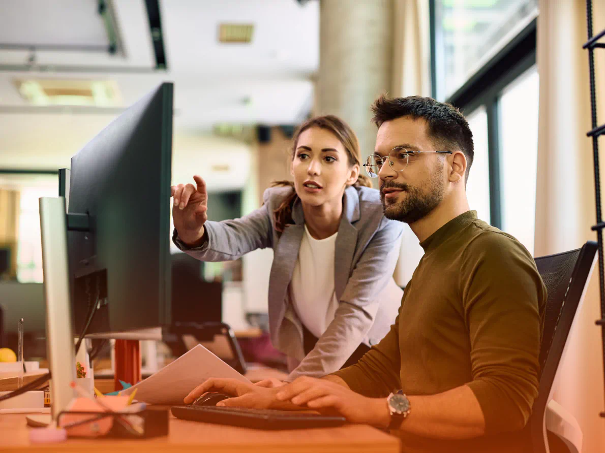 Two coworkers in discussion while using a desktop computer