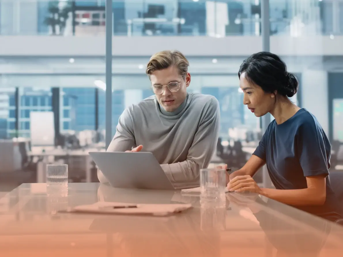 Man and woman sitting at conference table looking at laptop